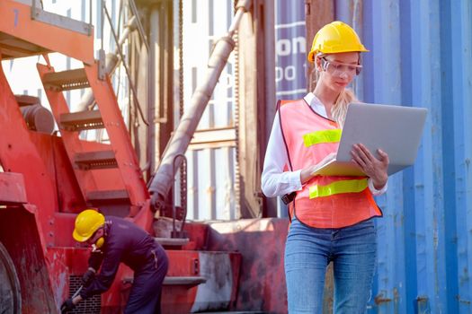 Beautiful technician or worker in cargo shipping area work with laptop and the other is working as background.