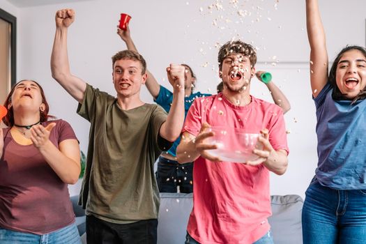 friends jumping for joy, throwing popcorn in the air after their team's victory. group of young people watching football at home. leisure concept. happy and cheerful. natural light in the living room at home. trumpet