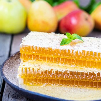 honey in honeycomb, close-up, on white ceramic plate, on wooden rustic table, side view, sunlight in sunny day.