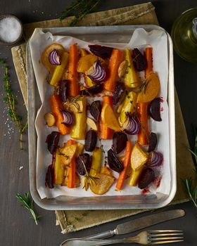 Colorful roasted vegetables on tray with parchment. Mix of carrots, beets, turnips, rutabaga, onions. Vegetarianism, veganism, proper nutrition, lchf. Top view, dark table
