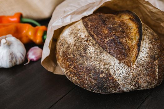 Freshly baked round loaf of sourdough bread on wooden table with vegetables. Artisan sourdough bread