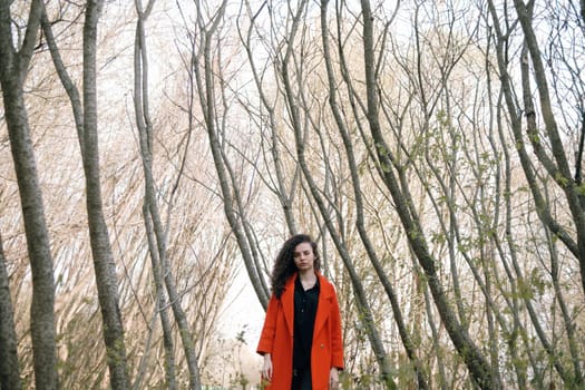 portrait of curly brunette woman in red coat in the park