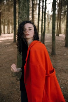 portrait of curly brunette woman in red coat in the park