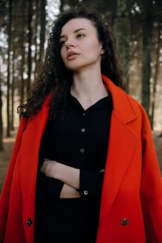 portrait of curly brunette woman in red coat in the park