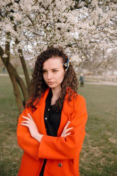 portrait of curly brunette woman in red coat in the park near flowering tree with ukrainian symbol in hair