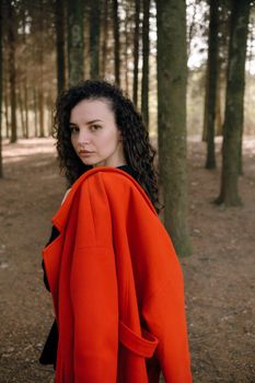 portrait of curly brunette woman in red coat in the park