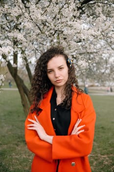 portrait of curly brunette woman in red coat in the park near flowering tree with ukrainian symbol in hair