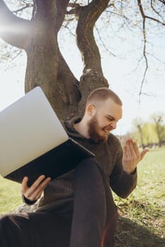 Young man using and typing laptop computer in summer grass.