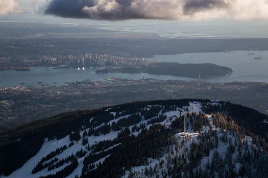 Aerial view of Grouse Mountain and Vancouver Downtown City, BC, Canada, in the background. Picture taken during a cloudy winter sunset.