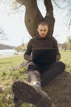 Young man using and typing laptop computer in summer grass.