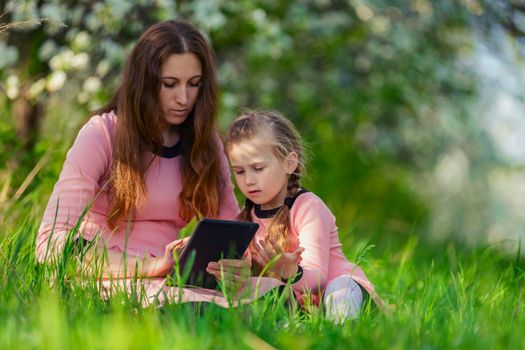 mother, with her daughter looking at the tablet on the background of flowering trees