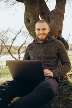 Young man using and typing laptop computer in summer grass.