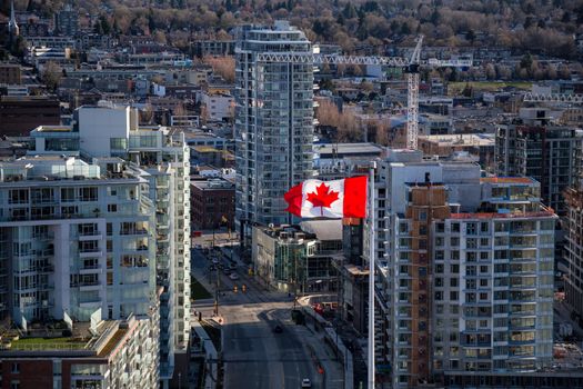 Aerial view of a Canadian Flag Flapping in the Wind with buildings and new construction in the background. Picture taken in Downtown Vancouver, British Columbia, Canada.