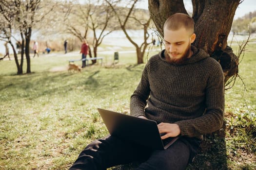 Young man using and typing laptop computer in summer grass.