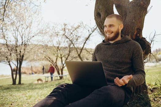 Young man using and typing laptop computer in summer grass.