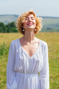 Beautiful blonde woman with short curly hair outdoors. Romantic model in summer white dress.