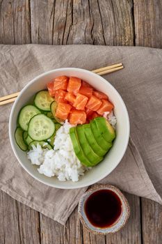 salmon poke bowl with fresh fish, rice, cucumber, avocado with black and white sesame. Food concept, top view, vertical