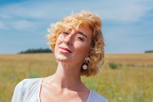 Beautiful blonde woman with short curly hair outdoors. Romantic model in summer white dress.