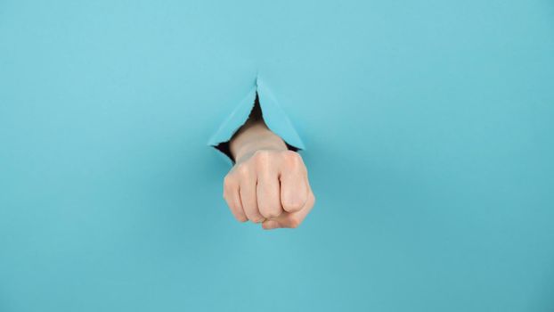A woman's hand sticking out of a hole from a blue background shows a fist
