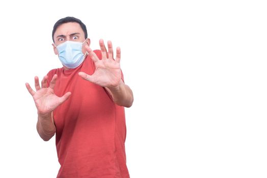 Fearful male in protective mask looking at camera with stop gesture while standing isolated on white background during coronavirus pandemic