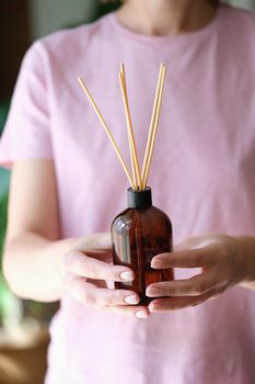 Close-up of woman holding aroma reed diffuser, home fragrance bottle with rattan sticks and smell of freshness