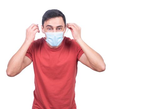 Content male putting on protective mask and looking at camera while standing isolated on white background during coronavirus outbreak in studio