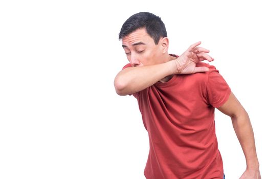 Sick man in red t shirt sneezing in elbow with closed eyes while standing isolated on white background in studio