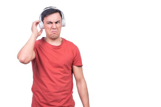 Isolated male model in red t shirt touching headphones unsatisfied with music on white backdrop