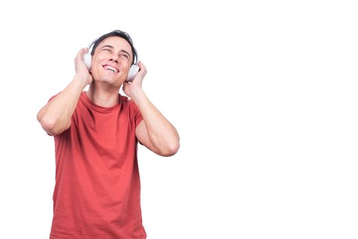 Positive guy in casual clothes enjoying music in wireless headphones while standing on white background in studio