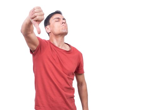 Haughty guy in red t shirt blinking eyes and demonstrating thumb down while standing on white backdrop