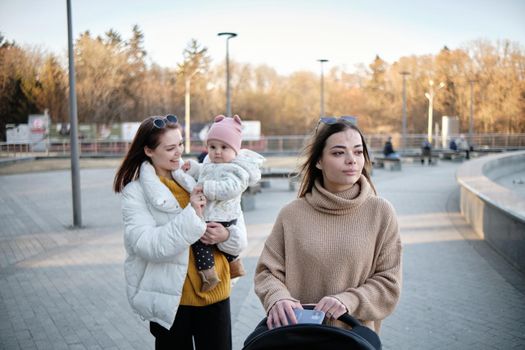 Smiling multi-ethnic lesbian couple walking outdoors with little son in baby carriage