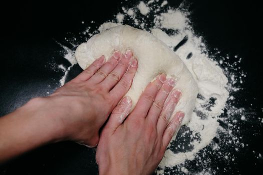 Pizza dough on a black table with hands and light