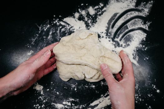 Pizza dough on a black table with hands and light