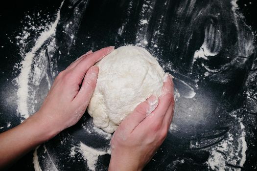 Pizza dough on a black table with hands and light