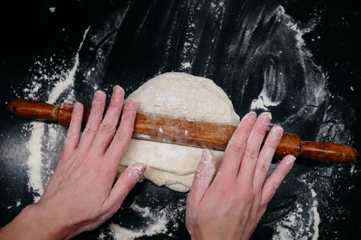 Pizza dough on a black table with hands and light