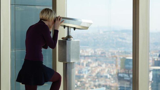 Woman tourist is looking through binoculars on city from a high point