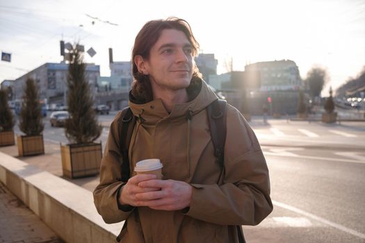 Happy smiling businessman going to the work with coffee cup and using modern smartphone outdoors, successful employer using cellphone while on break outside at sunny day near his office