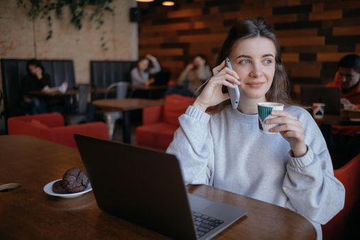 freelance woman happy working in a cafe remotely brunette and talking by the phone