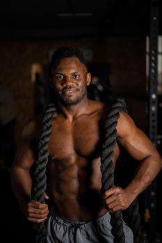 Muscular african american man posing with rope in gym