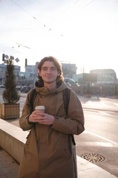 Happy smiling businessman going to the work with coffee cup and using modern smartphone outdoors, successful employer using cellphone while on break outside at sunny day near his office