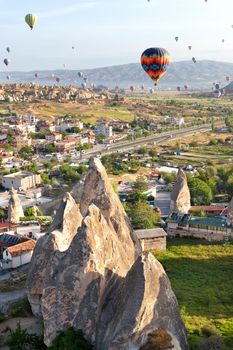 Sunny landscape of Goreme city with dozens of balloons flying in the sky of Cappadocia at sunrise in central Turkey.
