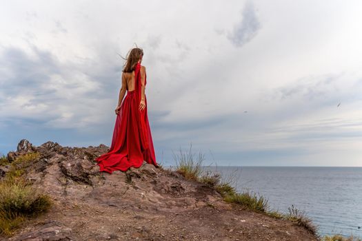 A woman in a red dress stands above a stormy sky, her dress fluttering, the fabric flying in the wind