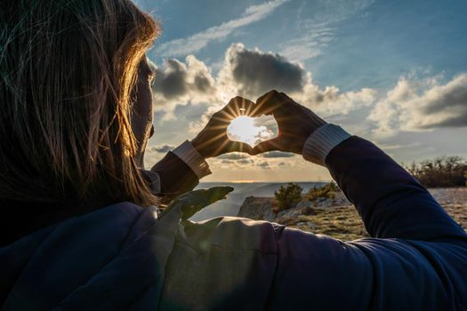 The girl made a beautiful heart from her finger in the rays of the sun. healthy woman making heart shape with hands at sunset. Shining summer sun on your hands. healthy heart concept