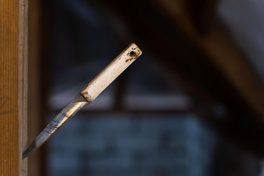 An old sharp knife with a plastic handle stuck into a wooden beam close-up in a dark room