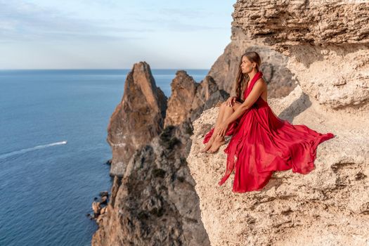 A girl with loose hair in a red dress sits on a rock rock above the sea. In the background, the sea. The concept of travel