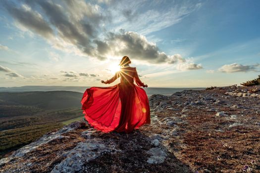 Rise of the mystic. sunset over the clouds with a girl in a long red dress. Stands on the mountain with a magical view