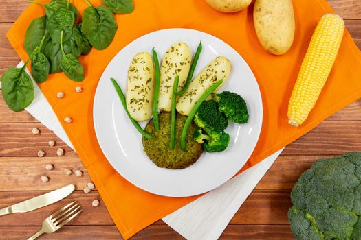 Top view of vegan burger or cutlet with baked potato, fresh green beans and vegetables on white plate.