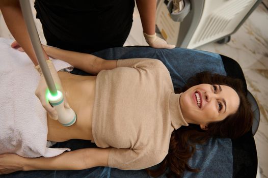 Top view of a young woman receiving microstimulation of the abdominal muscles, with a special radio frequency cavitation sensor in a spa clinic. Hardware cosmetology for skin care and body contouring