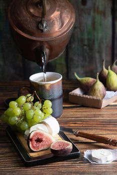 cheese plate with goat cheese, grapes and figs, copper teapot, angle view, healthy food, high-calorie breakfast. High quality photo