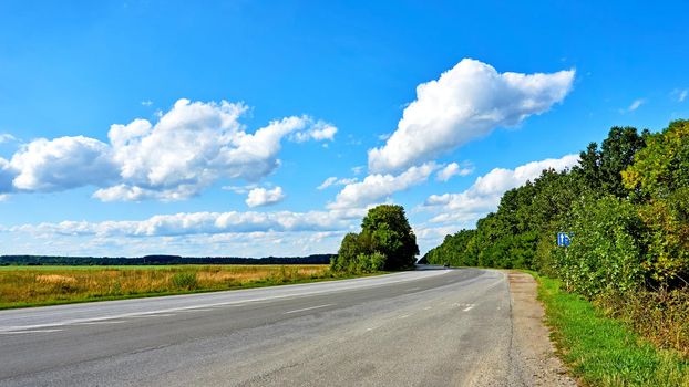 a wide way leading from one place to another, especially one with a specially prepared surface which vehicles can use.Asphalt road with fields and forest on the sides.